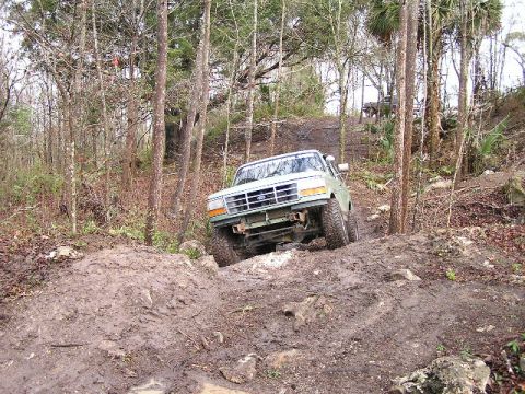 1994 Ford Bronco - 1994 Ford Bronco tackling a challenging muddy trail in a wooded area.