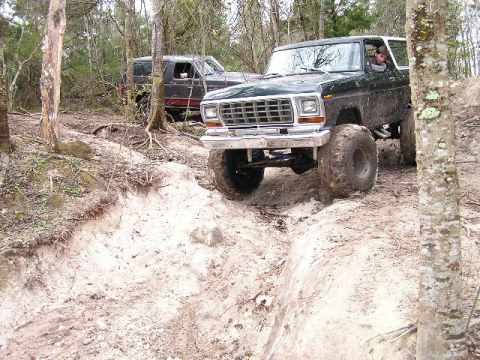 1994 Ford Bronco - Two SUVs navigating a muddy, wooded trail during an off-road excursion.