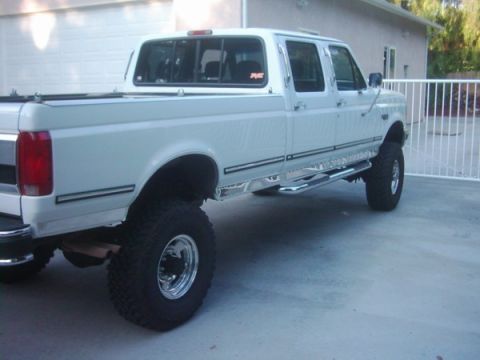 1978 Ford Bronco - This white crew cab pickup truck has large off-road tires and side steps.