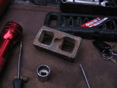1995 Ford Bronco - Tools and a rusty metal part are laid out on a brown surface, possibly for vehicle maintenance.