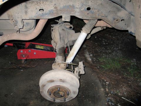 1995 Ford Bronco - Close-up view of the rear axle and suspension system of a vehicle, with a red jack supporting the frame.