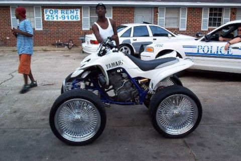 1996 Ford Bronco - A white Yamaha ATV with custom chrome wire wheels is parked in front of a building with police cars behind it.