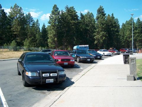 2001 Ford Crown Victoria - A dark sedan with a push bar and the license plate ADAM-12 is parked in a lot with other vehicles.
