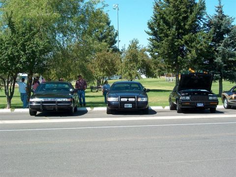 2001 Ford Crown Victoria - Three sedans parked on asphalt, one with hood open. The middle car has a push bar.