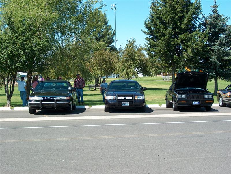 Three sedans parked on asphalt, one with hood open. The middle car has a push bar