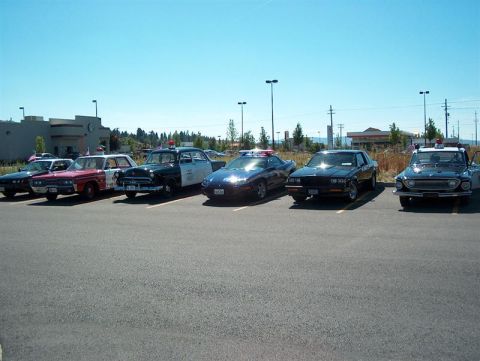 2001 Ford Crown Victoria - A collection of vintage and modern police vehicles are lined up in a parking lot.