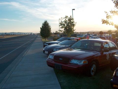 2001 Ford Crown Victoria - A line of vehicles, including a police car, are parked along a road at sunset.