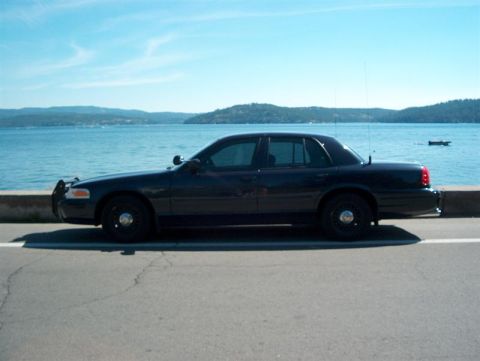 2001 Ford Crown Victoria - A dark 2001 Ford Crown Victoria is parked on the side of the road with a calm blue body of water in the background.