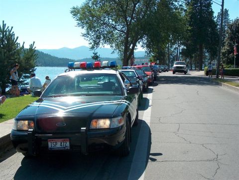 2001 Ford Crown Victoria - A line of vehicles, including a 2001 Ford Crown Victoria police car, parked on a street near a body of water.