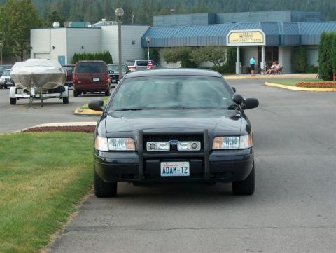 2001 Ford Crown Victoria - A black 2001 Ford Crown Victoria police car is parked in front of a conference center, with a boat trailer visible to the left.