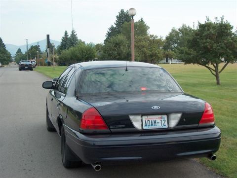 2001 Ford Crown Victoria - A black 2001 Ford Crown Victoria is parked on a residential street, with another vehicle visible in the distance.