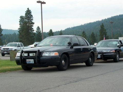 2001 Ford Crown Victoria - A black 2001 Ford Crown Victoria police car is parked in front of another police car, with a white pickup truck visible in the background.