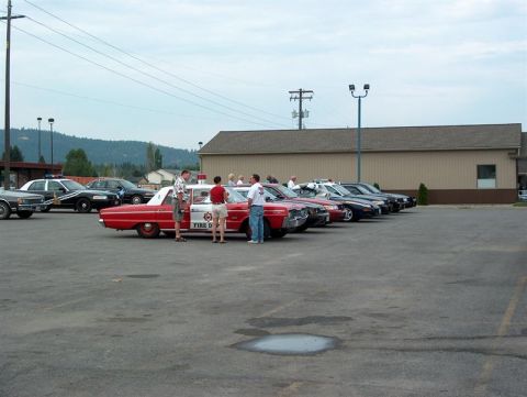 2001 Ford Crown Victoria - A gathering of vehicles, including a vintage fire department car and several police cruisers, parked in an outdoor lot.