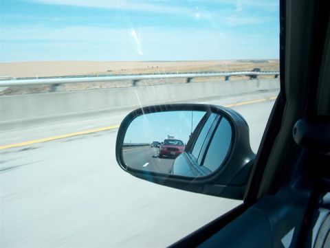 2001 Ford Crown Victoria - A red car is visible in the side mirror of a vehicle traveling on a highway.