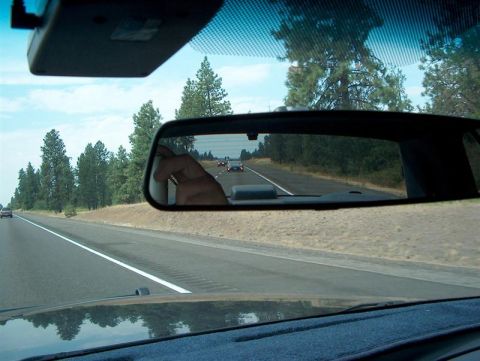 2001 Ford Crown Victoria - Highway driving scene reflected in the rearview mirror, showing traffic and trees.