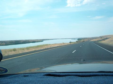 2001 Ford Crown Victoria - A view from the driver's seat of a car traveling on a highway alongside a body of water.