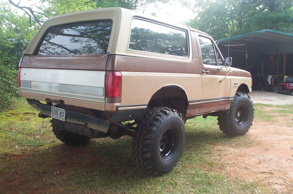 lifted 1987 Ford Bronco, brown and tan, parked on grass with a carport in the background