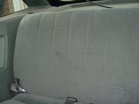 1989 Ford Escort - Interior view of a gray fabric rear seat with visible seatbelt buckles.