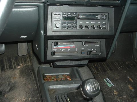 1989 Ford Escort - The interior of a car shows a manual transmission shifter, radio, and climate controls, with coins in the console.