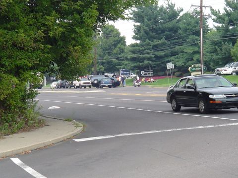 1993 Ford Bronco - A black sedan drives past a parking lot filled with various vehicles.