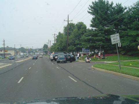 1993 Ford Bronco - A busy intersection scene with multiple vehicles, including a blue SUV, and pedestrians gathered near a sign.