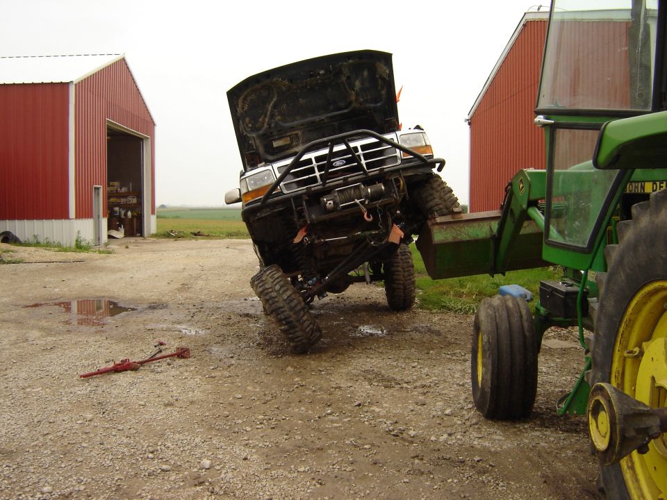 1992 Ford Bronco with hood open, lifted by a John Deere tractor loader