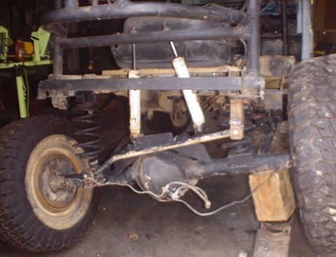 1989 Ford Bronco - The rear suspension and chassis of a modified off-road vehicle are visible, with a roll cage structure overhead.