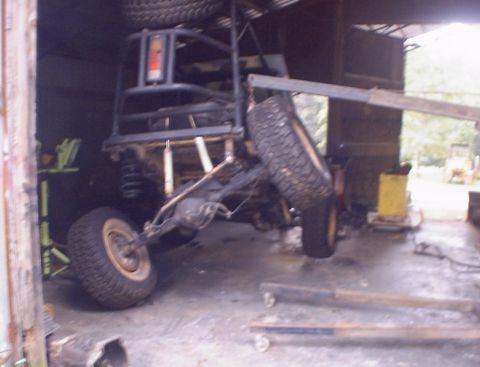 1989 Ford Bronco - The chassis of an off-road vehicle is suspended by a crane inside a garage.