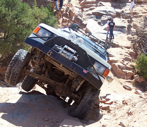 1990 Ford Bronco climbing a steep, rocky trail with its front wheels high off the ground