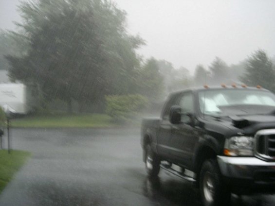Black Ford Super Duty crew cab in heavy rain on a wet driveway, camper trailer behind