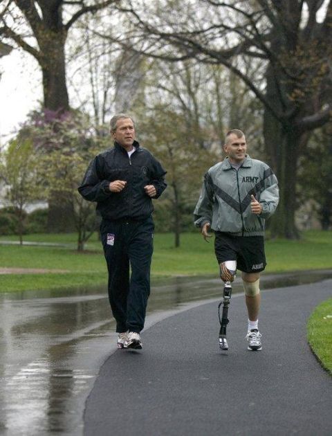 1986 Ford Bronco - A man with a prosthetic leg jogs alongside another man on a wet path in a park-like setting.