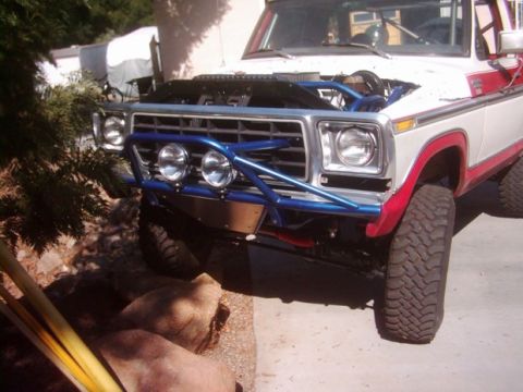 1978 Ford Bronco - The front of a white and red 1978 Ford Bronco is shown with its hood up and a custom blue bumper with lights.
