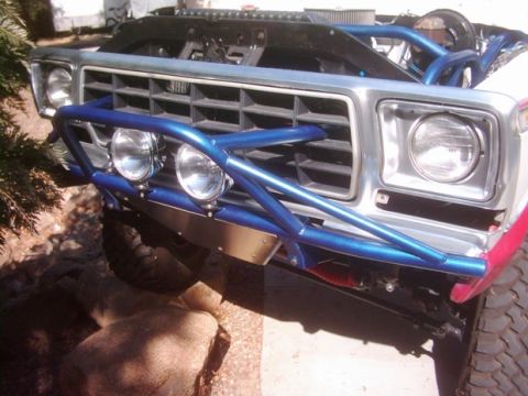 1978 Ford Bronco - Angled close-up of the front end of a lifted Ford 4x4 with a metallic-blue tubular prerunner bumper wrapping the silver grille, mounting tw…