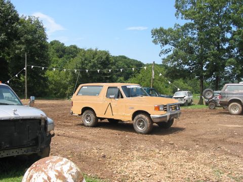 1988 Ford Bronco - A tan 1987 Ford Bronco sits in a muddy lot, with other vehicles visible in the background under a clear sky.