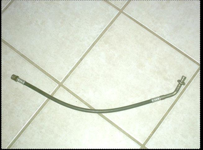 Curved metal hydraulic line with crimped fittings lying on a beige tile floor
