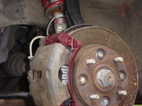 1998 Ford Taurus - Close-up of a car's brake system, showing a caliper and rotor with visible wear and a red painted bracket.