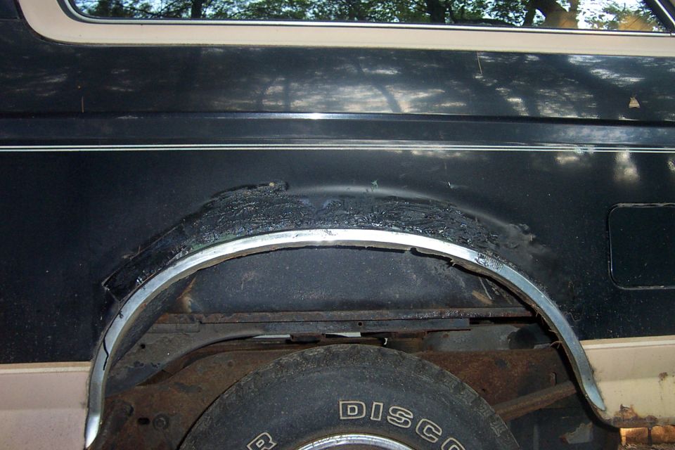 Rear wheel arch of dark SUV with flare removed, exposing rust and a spare tire