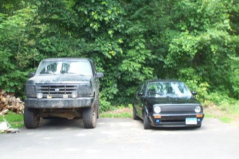 1996 Ford Bronco - A black 1992 Ford Bronco and a black Volkswagen Golf are parked side-by-side in front of a wooded area.