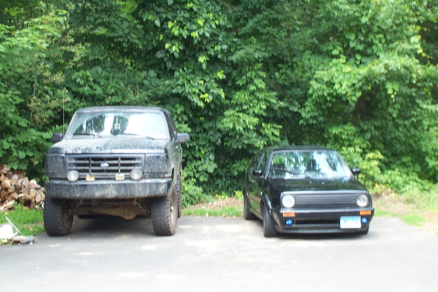 Front view of a black 1992 Ford Bronco parked next to a black Volkswagen Golf