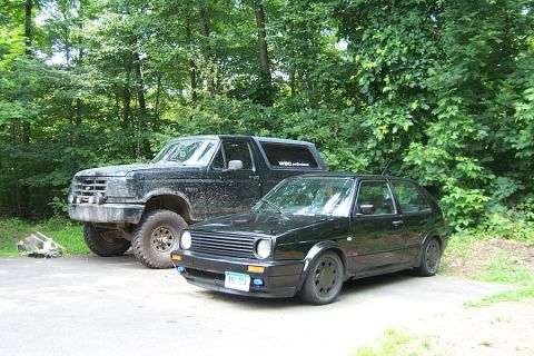 1996 Ford Bronco - Two cars, a Ford Bronco and a Volkswagen Golf, are parked next to each other in a wooded area.