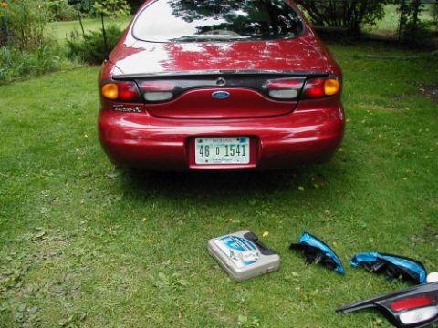 1997 Ford Taurus - The rear of a red 1997 Ford Taurus is shown with its tail lights removed and placed on the grass next to a toolbox.
