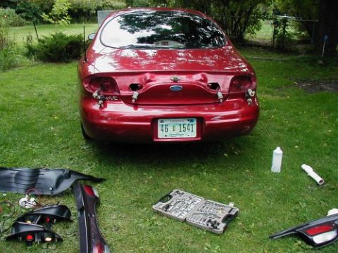 1997 Ford Taurus - The rear of a 1997 Ford Taurus is shown with its tail lights removed, with tools and parts laid out on the grass.