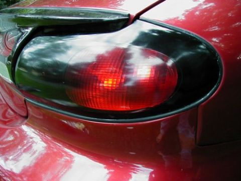 1997 Ford Taurus - Close-up of the driver-side oval tail light on a red Ford Taurus sedan, its clear reverse and outer sections blacked out so only the red br…