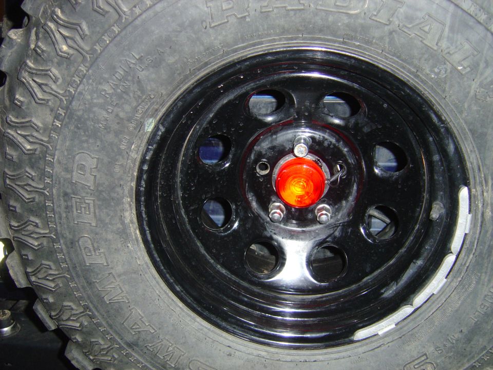 Black steel wheel with mud-terrain tire and orange lens in center hub