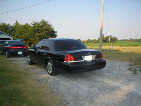 1987 Ford Crown Victoria LTD - A black sedan is parked on a gravel driveway next to another car, with a field in the background.