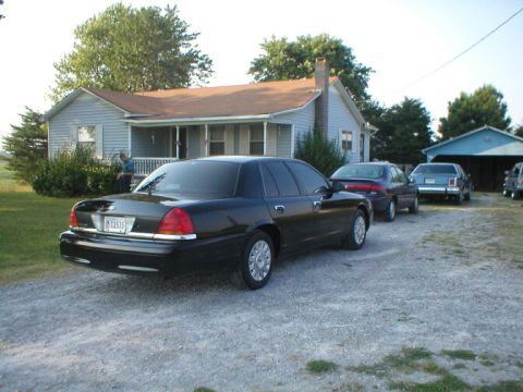 1987 Ford Crown Victoria LTD - Several cars are parked in a gravel driveway in front of a house and garage.