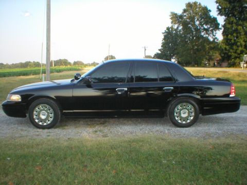 1987 Ford Crown Victoria LTD - This black sedan, likely a Ford Crown Victoria from the early 2000s, is viewed from its side profile.