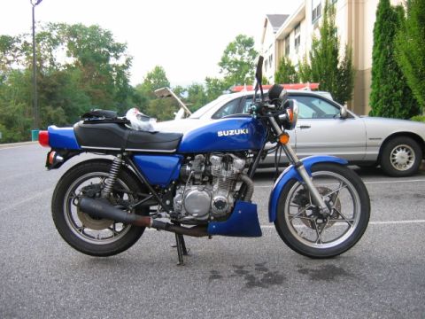 1985 Ford Crown Victoria LTD - A blue Suzuki motorcycle is parked in front of a silver sedan.