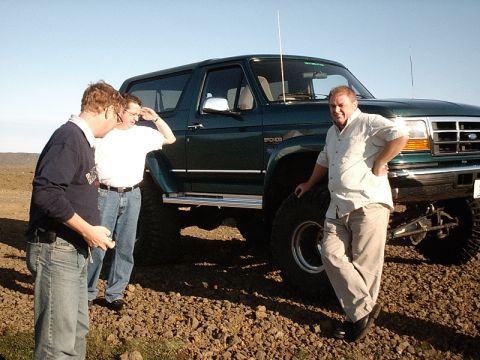 1996 Ford Bronco - A dark green 1996 Ford Bronco is shown with a lifted suspension and oversized tires, accompanied by three men on a sunny day.