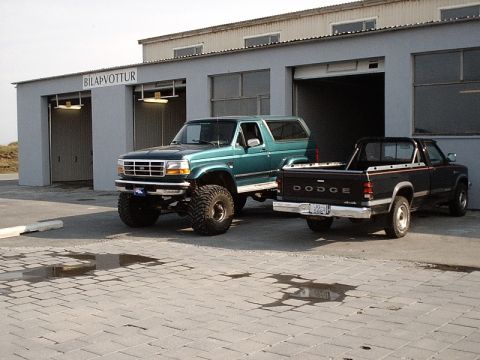 1996 Ford Bronco - A lifted green 1996 Ford Bronco is parked in front of a building with a black Dodge pickup truck beside it.